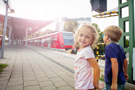 On a railway station, young boy and girl look at commuter trainの写真素材
