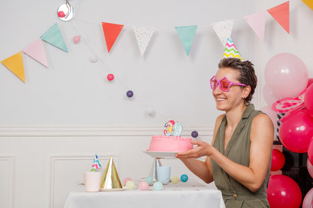 Happy woman make birthday wish hold cake in bright living roomの写真素材