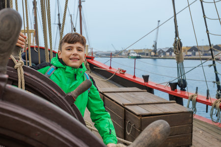 Teenager in a vibrant green coat joyfully holding ships wheelの写真素材