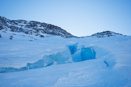 Deep blue crevasse spliting the snowy landscape and icy hillsの写真素材