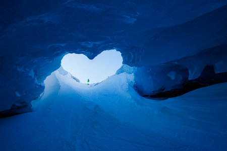 Ice cave with heart-shaped entrance offer view of a clear sky