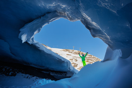 Boy skier stand at entrance of majestic blue ice cave landscapeの写真素材