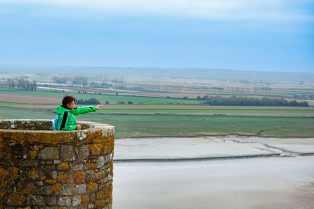 Young boy in green gear enjoying the view from a stone wallの写真素材