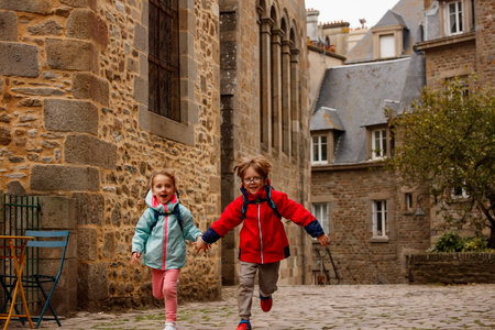 Kids with backpacks joyfully run on a historic cobblestone pathの写真素材