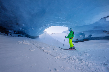 Skier teenager explores stunning blue ice cave in bright outfitの写真素材