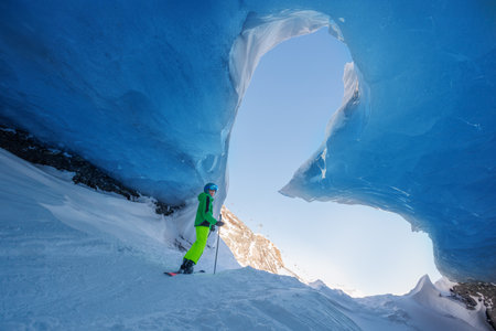 Skier boy exploring stunning ice cave with bright blue ceilingの写真素材