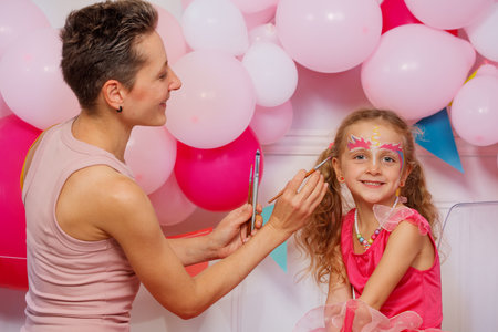 A girl beams with joy as an adult woman applies unicorn makeup