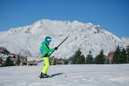 Teen skier boy on a tow lift in front of snowy mountain peaksの写真素材
