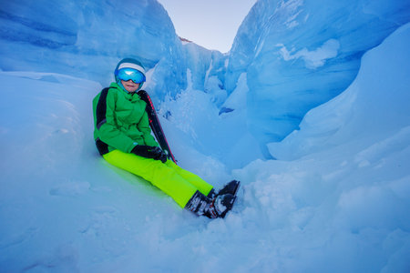Person in bright ski outfit sitting at a stunning ice canyonの写真素材