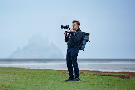 Man equipped with a camera films hazy Mont Saint Michel castleの写真素材
