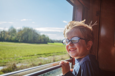 Boy leans from carriage window taking in green fields passing by