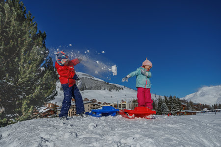 Little boy and girl having fun fight with snowballs on a hillの写真素材
