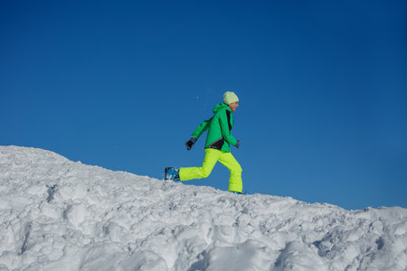 Happy teenage boy running on snowy hill, blue sky backgroundの写真素材