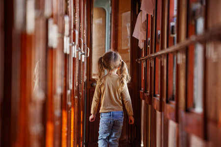 Young girl strides confidently down narrow wooden train corridorの写真素材