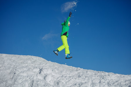 Energetic teenager boy jump under clear blue sky on snowy hillの写真素材