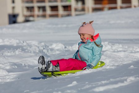 Girl in teal coat slides alone on green sled down a snowy hillの写真素材