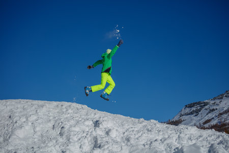 Happy teen boy in bright gear run over snowy slope at mountainsの写真素材