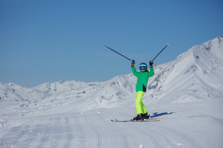 Skier in neon green jacket lifts poles overhead on sunlit slopeの写真素材