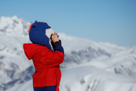 Boy with binoculars surveys snowy mountain scenery in binocularの写真素材