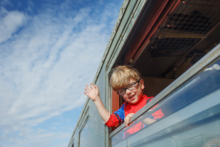 Boy waves cheerfully from green coach window at bustling stationの写真素材