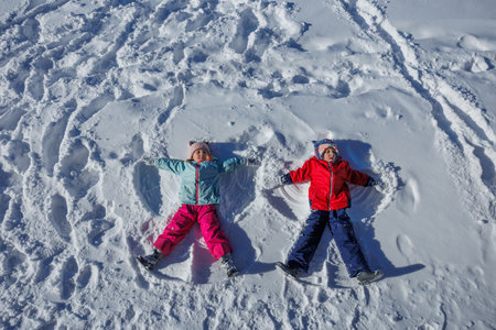 Two kids are making snow angels dressed in colorful winter gear