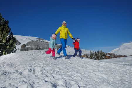 Dad in neon green leads two kids running across a snowy field