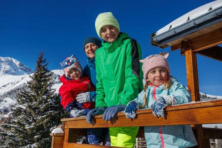 Family of four stands by snowy balcony railing under clear skyの写真素材