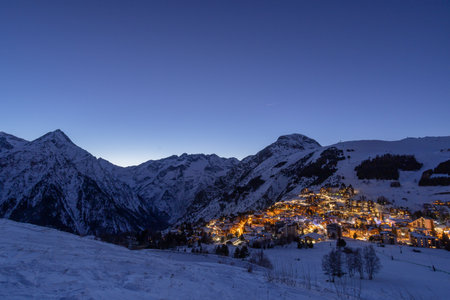 Twilight alpine village lights against snow-covered mountainsideの写真素材