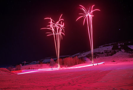 Pink firework bloom over snow winter slope under clear night skyの写真素材