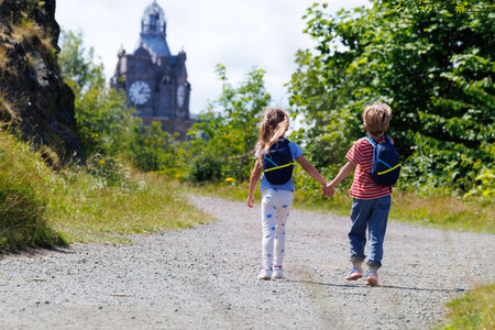 Two kids with backpacks walk towards a clock tower, Edinburgの写真素材