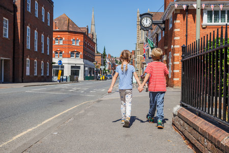 Two children walk hold hands on bright, sunny day, Farnham, UK