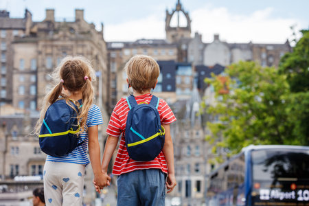 Children gaze at city traffic, holding hands with backpacks onの写真素材
