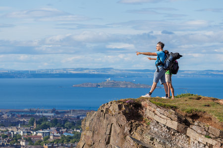 Two hikers marvel at expansive views from a grassy cliff edgeの写真素材