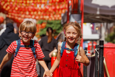 Kids with backpacks walk joyfully under vibrant red lanternsの写真素材