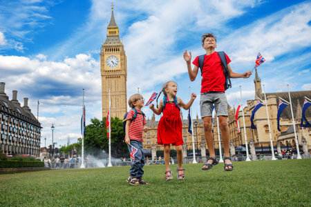 Group of kids tourists jump joyfully near Big Ben with UK flagsの写真素材