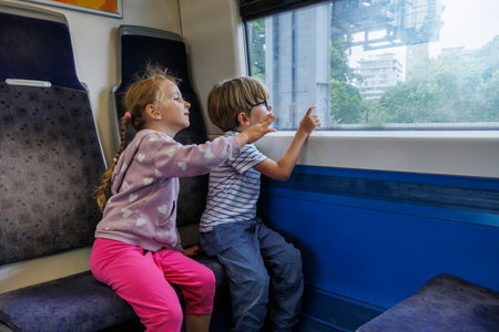 Girl and boy in train car seat pointing at window enjoy ride