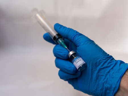 A doctor holds a syringe aspirating a dose of a recently developed COVID-19 vaccine ready to inject in a patient's arm in order to provide immunity against this condition trying to collaborate to stoの写真素材
