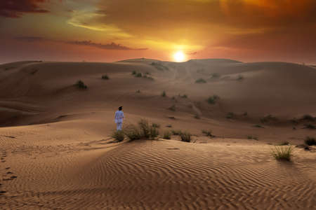 Beautiful desert landscape during sunset and golden hour with very dramatic sky with a person walking between dunesの写真素材