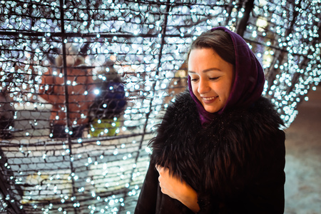 Young woman in warm clothes standing near Christmas decorations looking down and smilingの写真素材