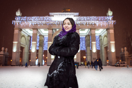Young and cute woman standing under snowing in the park in winter timeの写真素材