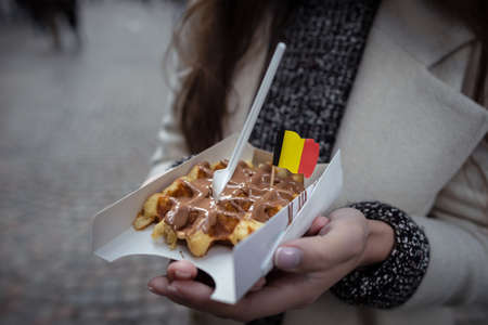 Belgian waffles decorated with the national flag in the young woman hands. Close up view. Hands holding fresh waffles with milk chocolate.の写真素材