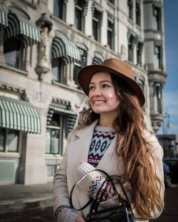 Portrait of a young woman. Trendy woman with a smile looking on buildings and touring old town. Beautiful girl walks in Rotterdam, Netherlands.の写真素材