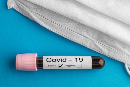 Covid-19 positive blood test sample with protective face mask isolated on blue background. Coronavirus concept and background.の写真素材