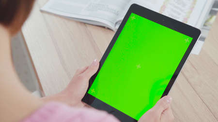 Working with a tablet computer: a green screen and a tablet in the hands of a young woman. It touches the screen, mimics the flipping. Taken over the shoulder, only the tablet and hands in the frame.の写真素材