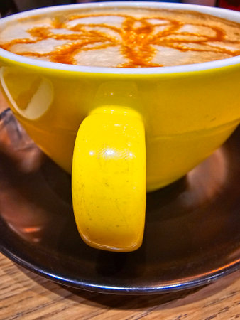 Hot latte art coffee in a yellow cup on wooden table.