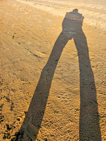 Shadow of a man standing on the sand in the evening sun.