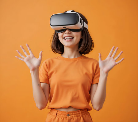 Cheerful young woman wearing virtual reality goggles and gesturing while standing against orange backgroundの素材