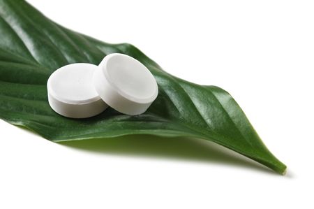white pill lying on a green leaf isolated on a white backgroundの写真素材