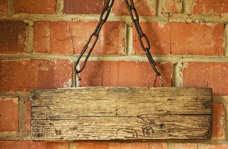 old wooden sign on a chain on the background of a brick wallの写真素材