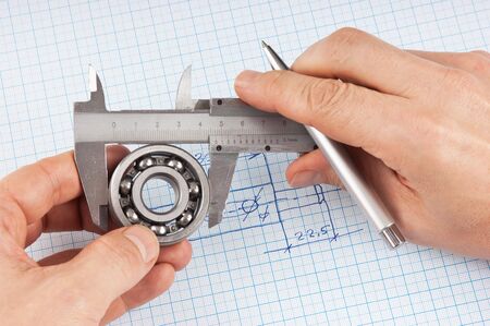 Technical drawing and callipers with bearing in hand on graph paperの写真素材